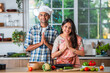 Indian asian couple promoting, showing or holding kitchen utensils in kitchen