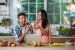 Happy Indian asian smart couple having fun in kitchen using laptop while cooking