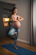 A full length shot of a happy pregnant woman practicing yoga at home and balancing her weight