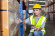 Female worker looking at camera wearing safety uniform and hard hat using tablet checking inspect goods on shelves in warehouse. women worker check stock inspecting product in factory.