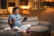 A happy pregnant woman ordering and shopping online using a tablet and a credit card