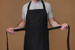 Man wearing kitchen apron on brown background, closeup. Mockup for design