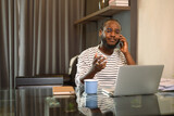 Fototapeta Nowy Jork - Young African man having serious phone conversation and working with laptop at home