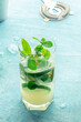 Mojito cocktail. Summer cold drink with lime, fresh mint, and ice. Cool beverage on a blue background, with a strainer