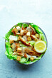 Caesar salad with chicken breast, lettuce, croutons, and a lemon, top shot on a slate background
