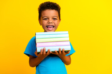 Sticker - Portrait of positive small schoolboy with afro hair wear blue stylish t-shirt hold book smiling isolated on vivid yellow background