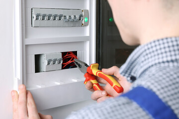 Canvas Print - Professional repairman fixing electric panel with pliers indoors, closeup