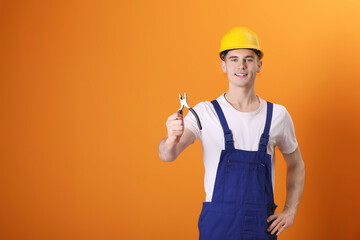 Wall Mural - Young man holding pliers on orange background, space for text