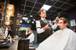 Experienced hairdresser styling client's hair. Handsome hairstylist in fancy outfit at work. Male barber using professional hairdryer and brush.