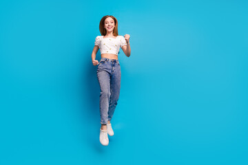 Wall Mural - Full length portrait of lovely girl jump raise fist empty space wear top isolated on blue color background