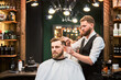 Hairdresser making final touches in new haircut. Comfortable atmosphere in modern barbershop. Stylish barber using professional comb to style hair.