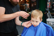 Hairdresser using electric shaver to cut boy's hair. Little kid getting first haircut in barbershop. Close up