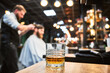 Close-up photo of a glass of whiskey. High-quality barbershop offering drinks to customers. Glass with alcohol on the background of hairstylist making haircut.