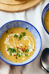 Wall Mural - Two bowls of creamy potato soup, spoons, napkin and wooden cutting board with a loaf of bread and cut pieces. The surface of the soup is decorated with cream, croutons, parsley and ground red pepper.