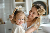 Fototapeta  - Caucasian mother brushing hair with hairbrush baby toddler. Cosy bathroom with natural light, mom and child happy and playful atmosphere. Hygiene for children, childcare. Daily routine