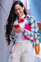 Vertical portrait Happy young latin woman browsing the internet using mobile device outdoors.