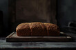 A loaf of bread with sesame seeds on top sits on a wooden cutting board. Dark background