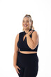 Caucasian young plus-size woman in black sportswear stands, smiling on white background