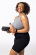 Biracial plus size model with yoga mat and water bottle, smiling, white background
