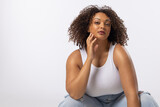 Fototapeta  - A biracial young female plus size model sits on white background, copy space