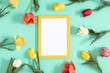Festive floral background. Beautiful tulip flowers and yellow empty photo frame on a pastel mint background. Top view, flat lay.