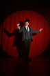 Magician with pigeon standing over red drapery in spotlight