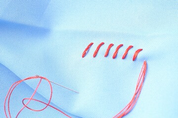 Poster - Sewing needle with thread and stitches on light blue cloth, closeup