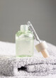 Opened cosmetic bottle with green serum on folded grey bath towel close up