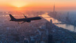 A large jet is flying over a city at sunset. The sky is orange and the sun is setting. The city below is lit up with lights, creating a warm and inviting atmosphere