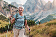 © mendor - An elderly woman with white hair smiles brightly as she hikes with trekking poles in a mountainous landscape