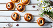 Round butter buns with raisins, a bunch of white flowers on a white wood plank background