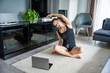 Young woman in sportswear doing yoga exercises on mat in living room. Online workout, fitness, practicing and meditation at home