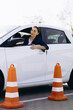Woman sits in car , driving back and looking at the cones set up close to car