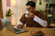 © DragonImages - Young man drinking morning coffee and checking emails on laptop