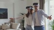 A young couple in VR glasses stands with their arms outstretched in the room.