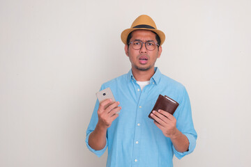 Wall Mural - A man showing confused expression while holding mobile phone and wallet