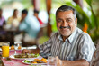 © AI_images - An enthusiastic Indian man delights in his breakfast at the hotel, smiling at the camera with a sense of satisfaction and contentment as he enjoys his meal.