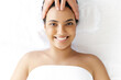 Top-view on calm relaxed smiling brazilian or hispanic young woman lies on a massage table in a salon during a forehead massage.Female massage therapist doing general forehead massage to a pretty girl