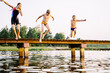 Teen girl in swimsuit and two smaller boys jumping from a bridge into a lake at sunset. Happy summertime, healthy childhood, sport concept.