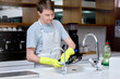 Cleaning, washing and plate for man in home kitchen, gloves and hand or apron for safety. Dirty, dishes and hygiene with soap for bacteria prevention, germs and disinfect crockery for ocd male person