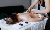 Fototapeta Młodzieżowe - Woman enjoying hot stone massage at spa salon. Professional masseur making stone therapy. Relaxing and ease tense muscles and damaged soft tissues throughout body.