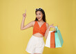 Happy sexy young woman dressed in swimwear holding shopping bag shopping in summer sale on yellow background.