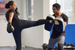 © peopleimages.com - Boxer, woman and trainer with boxing kick for fight workout of muay thai exercise for self defense. Fitness coach, athlete and sport pads for strength and power training in gym with cardio instructor