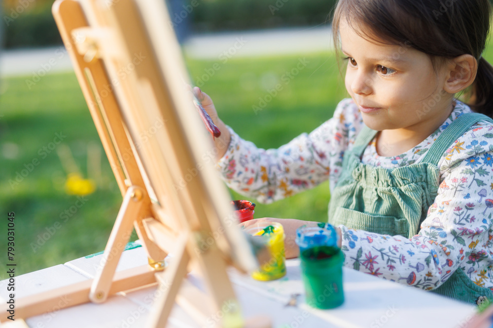 Little girl is painting a picture in the park on the green grass. Child ...