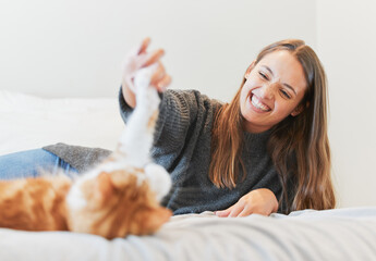 Poster - Playing, smile and woman with cat in bedroom of home for bonding or love as pet owner. Bed, happy or toys and person having fun with adorable kitten in apartment for morning or winter relaxation