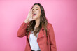 Young beautiful woman wearing casual jacket over isolated pink background shouting and screaming loud to side with hand on mouth