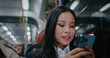 Asian girl talking on smartphone with friend or family member. Commuting back home in evening on train or subway. Using mobile device for remote communication. Ending discussing before hanging up.