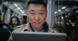 Frontal view of Chinese man traveling in public transport. Going home after work in evening. Light flickering in window outside. Male using tablet device or laptop. Actively searching for information.