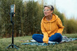 a pretty blogger girl in glasses and an orange hoodie is sitting in a park in nature, streaming on her phone and emotionally chatting with subscribers, expressing kind emotions