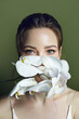 Portrait of a beautiful young fair-skinned woman with green eyes. Woman with white flowers.White orchid in front of a girl’s face. Advertising of face and skin care products. Ideal young facial skin.